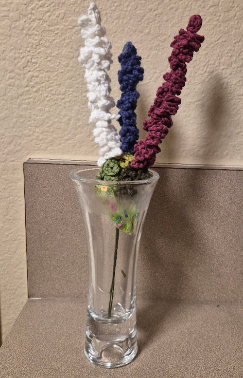 Three cotton yarn lavender stems in white, deep blue and burgundy displayed in a clear vase; vase not included
