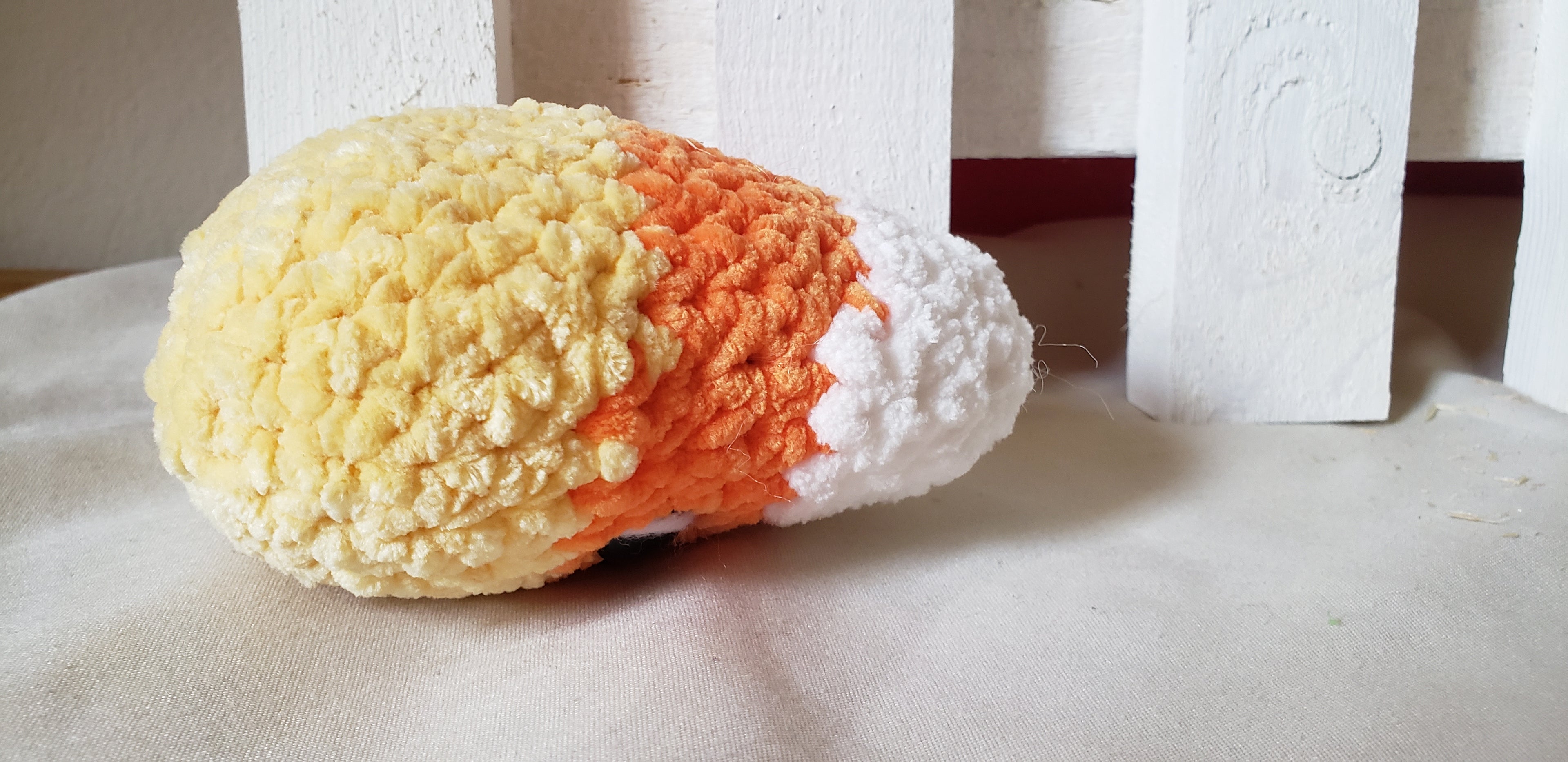 Crochet candy corn plushie laying on side showing full profile and color detail