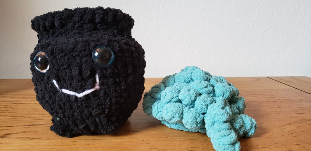 Mini crochet cauldron assembled with turquoise bubbling liquid lid and smiley face, side view