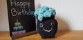 Mini crochet cauldron with turquoise bubbling liquid and glitter eyes next to Happy Birthday chalkboard sign