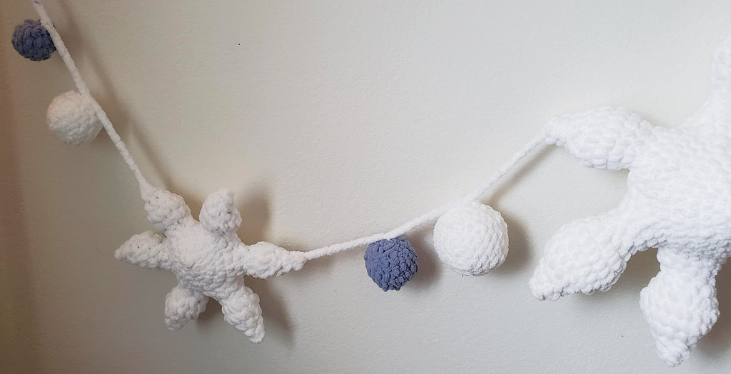 Crochet plush snowflake garland close-up showing mini snowflake and plush ball detail in white and slate blue