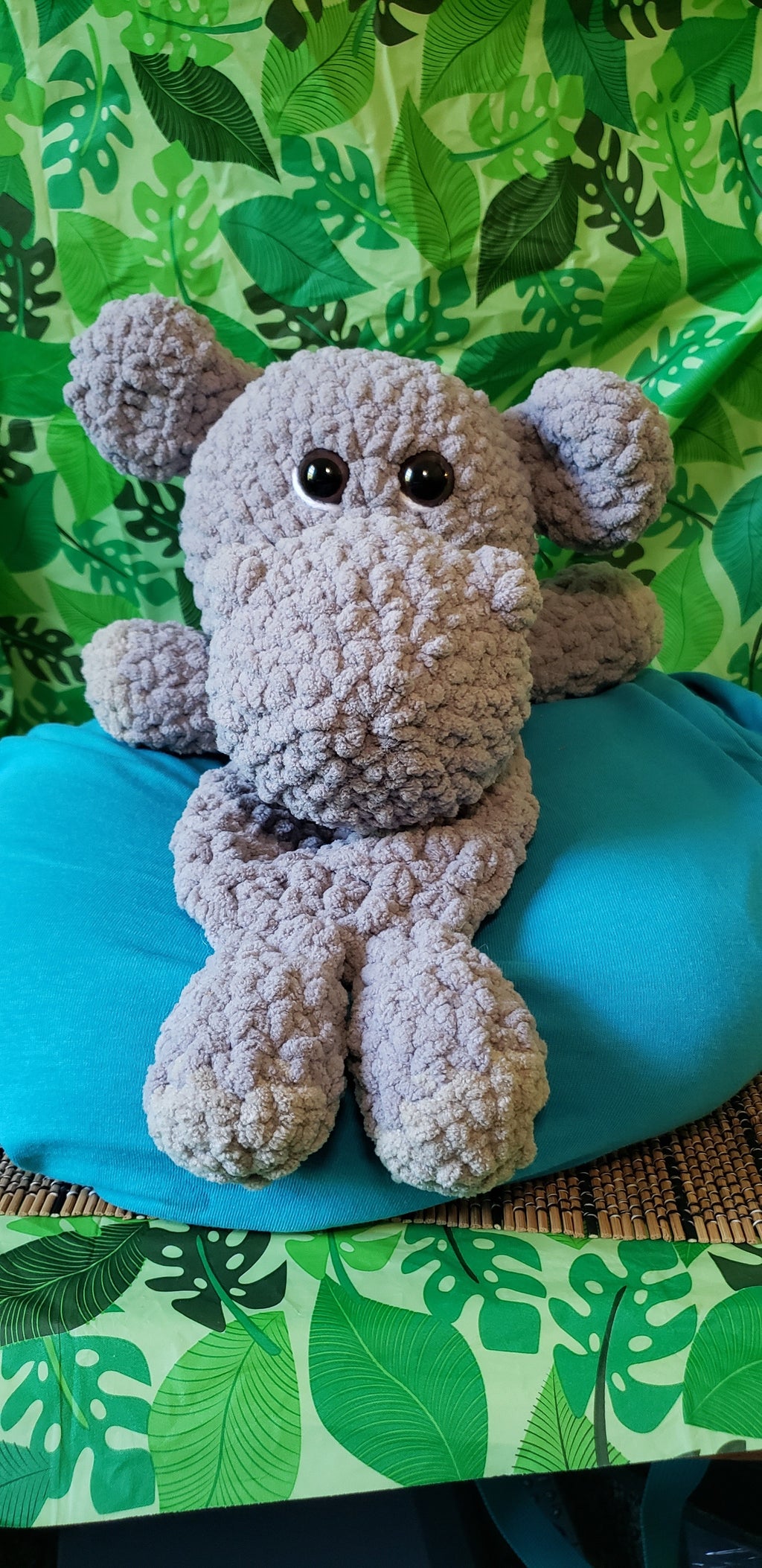 Front view of crocheted gray hippo snuggler on teal pillow
