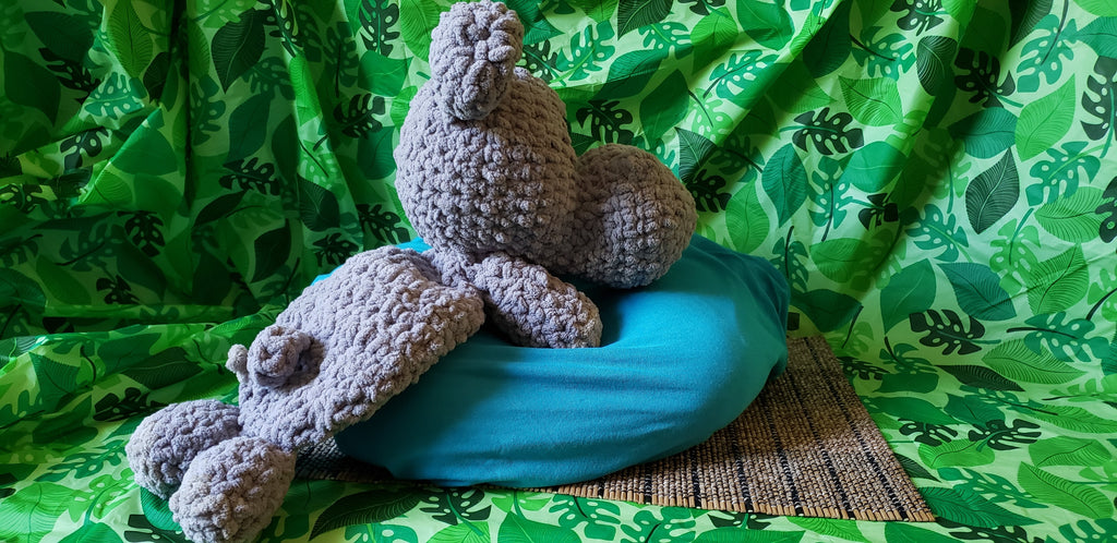 Side view of crocheted gray hippo snuggler on teal pillow