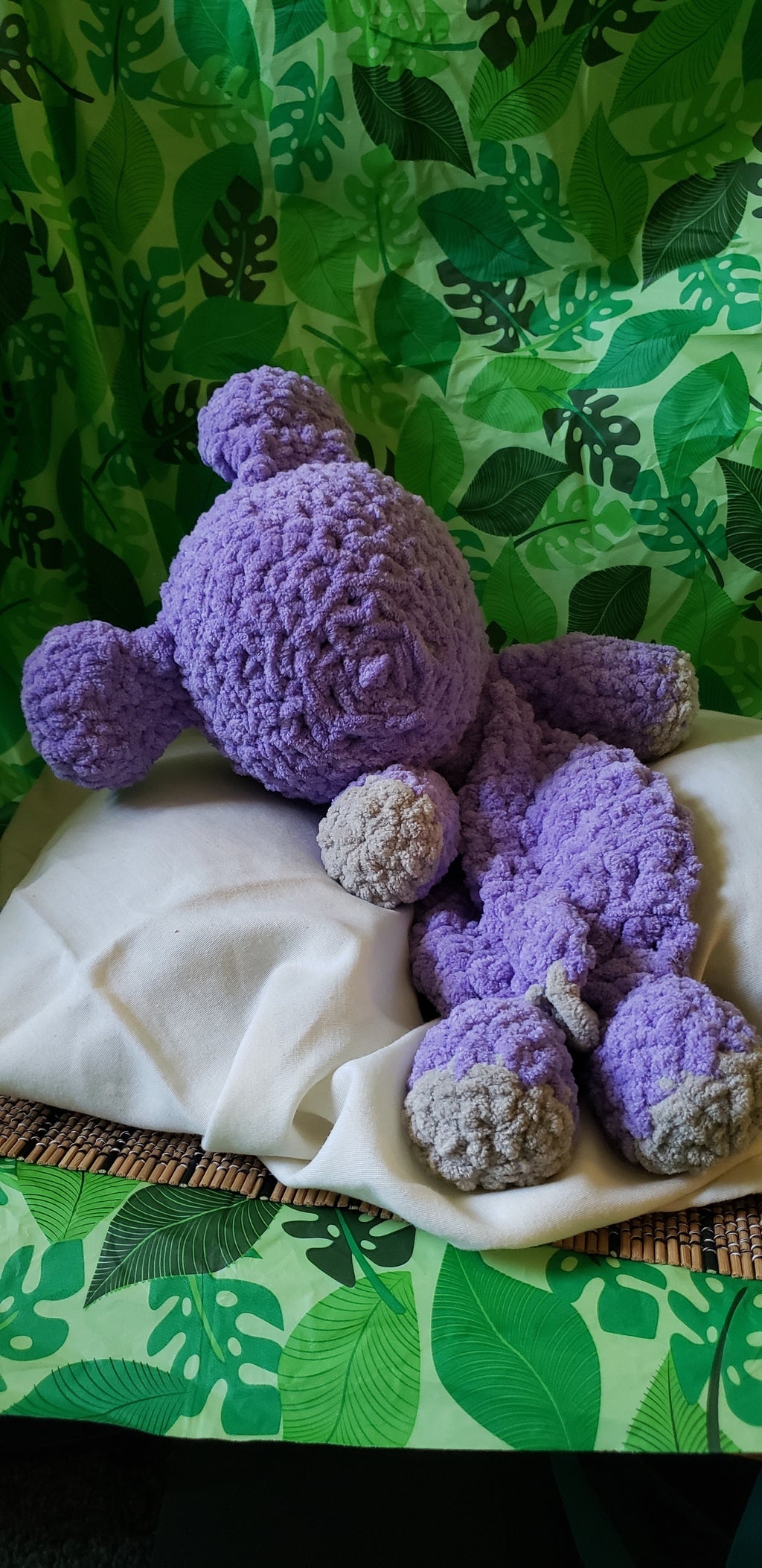 Back view of purple crocheted hippo snuggler on white blanket