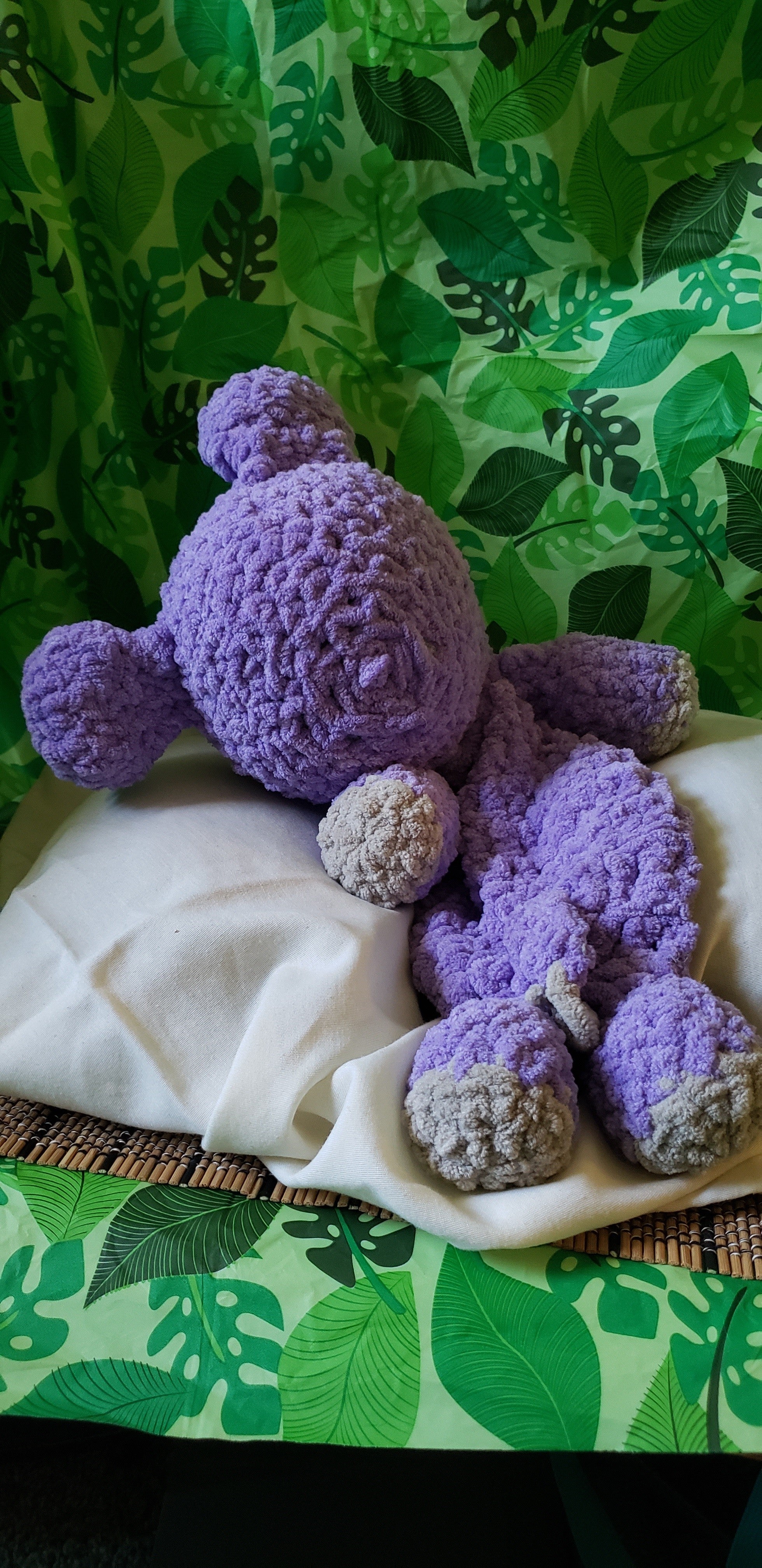 Back view of purple crocheted hippo snuggler on white blanket