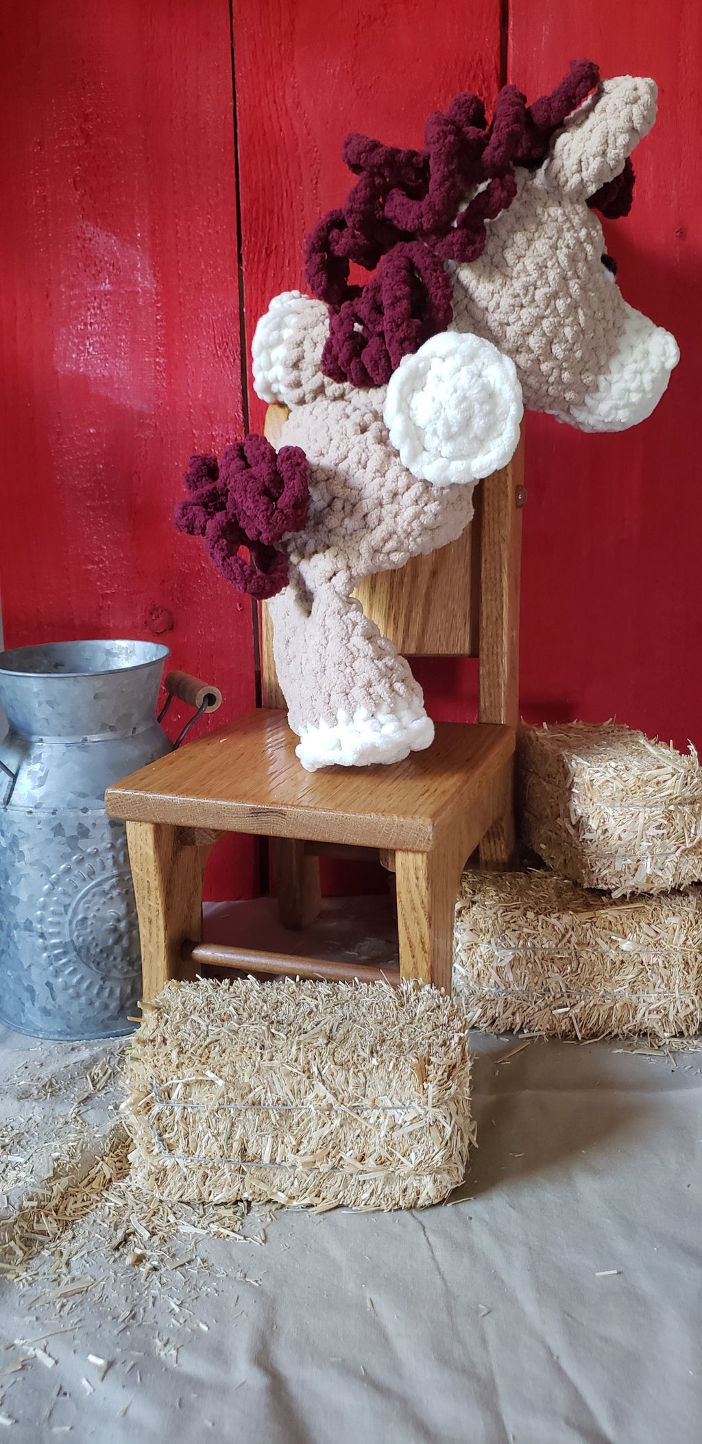 Back view of tan crocheted pony plushie with burgundy mane on wooden chair