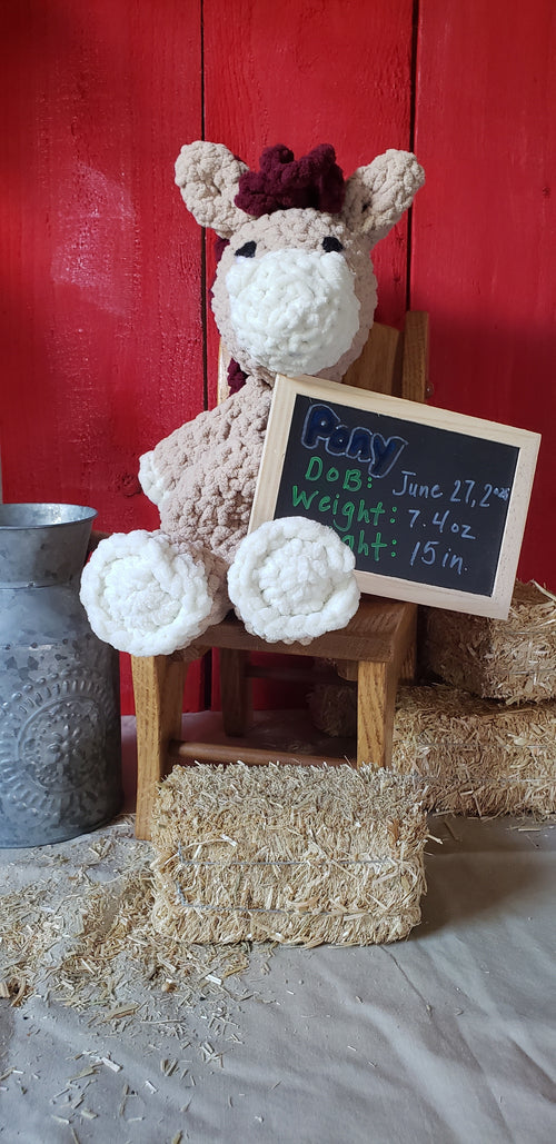Tan crocheted pony plushie with burgundy mane holding birth announcement chalkboard sign