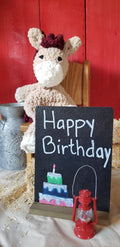 Tan crocheted pony plushie with Happy Birthday chalkboard sign in barn setting