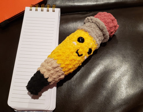 Handmade crochet pencil plushie with happy face, yellow body, gray ferrule, and pink eraser, approximately 9 inches long