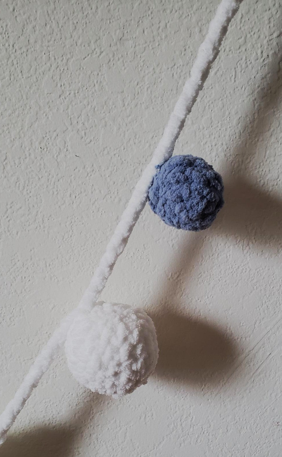 Crochet plush snowflake garland close-up detail of white and slate blue plush balls on white yarn strand