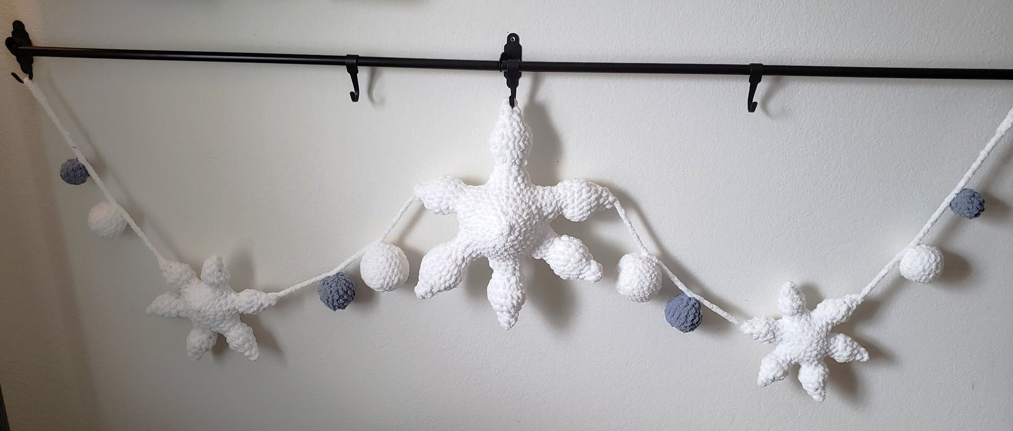 Crochet plush snowflake garland full length view showing 1 large center snowflake, 2 mini snowflakes and 8 plush balls in white and slate blue