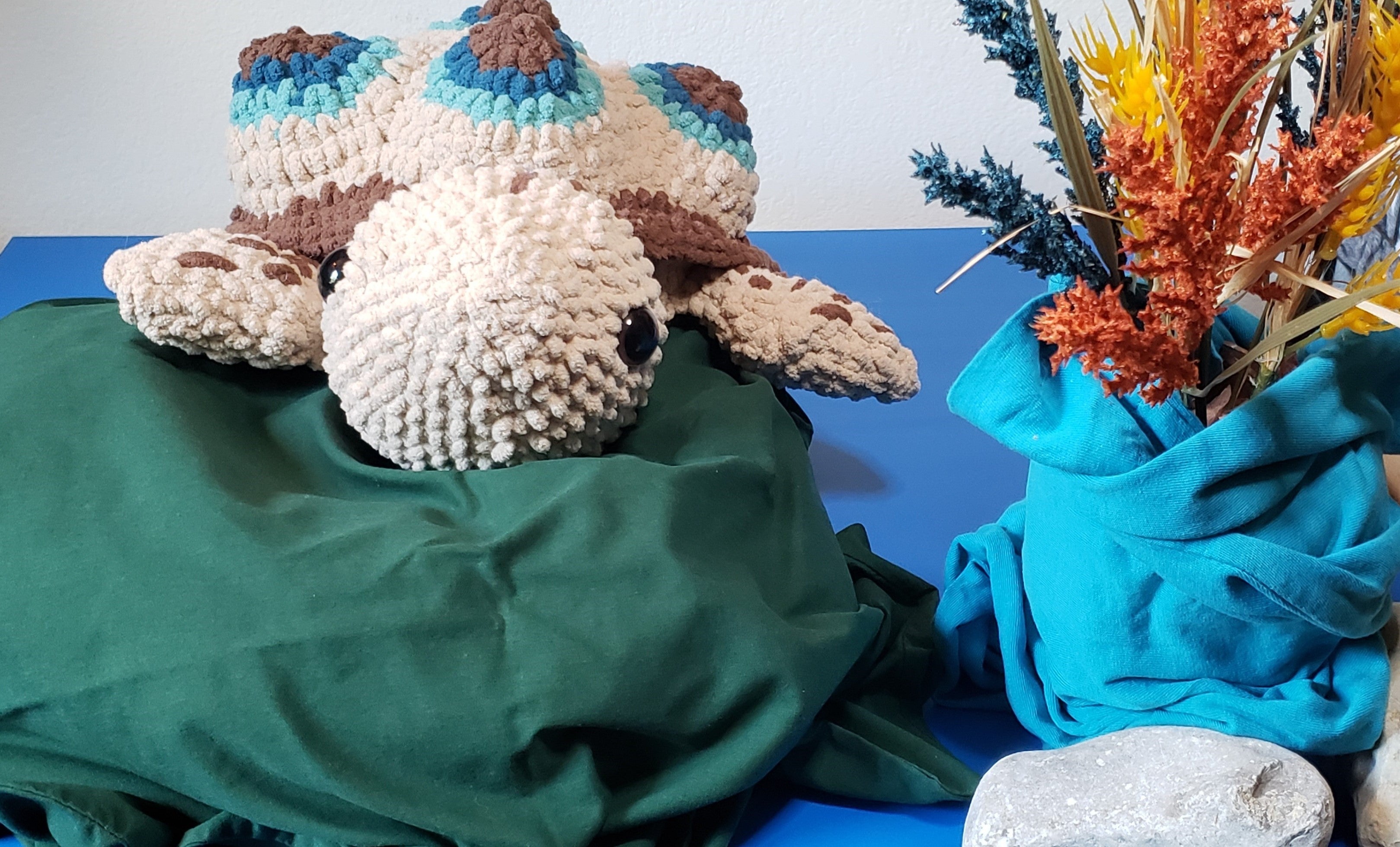 Crochet turtle plushie front facing on green lily pad with dried flowers